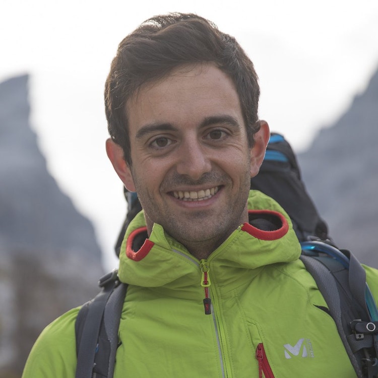 A lansdcape image of Stefano Bernadi in a bright green hiking jacket up a mountain